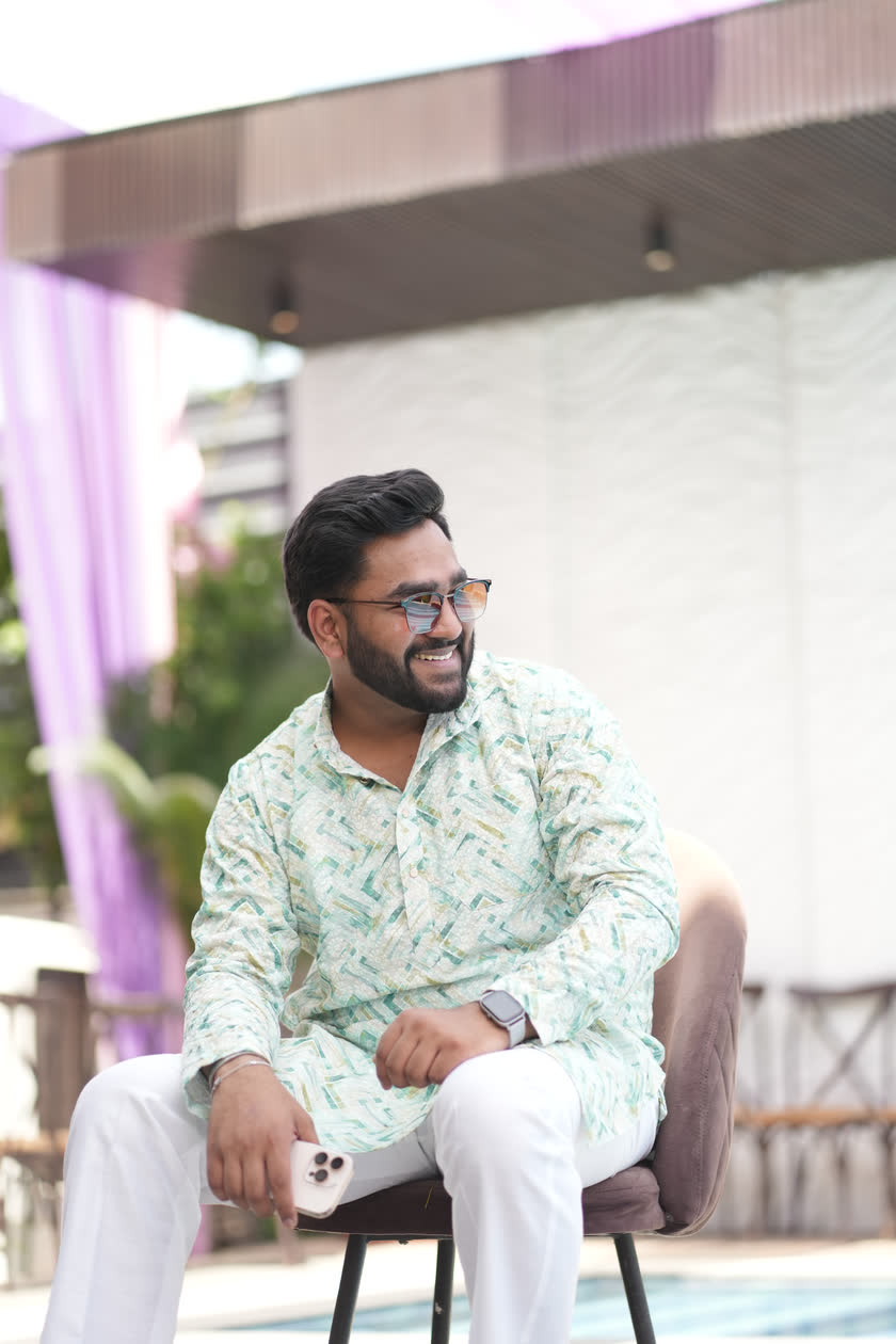 Harsh Agarwal seated outdoors, laughing, in a patterned kurta and sunglasses