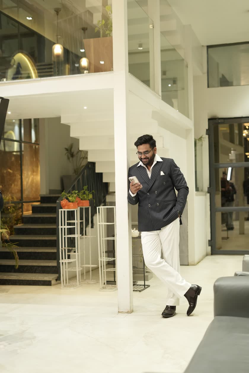 Harsh Agarwal in a pinstripe suit, leaning on a pillar and checking his phone